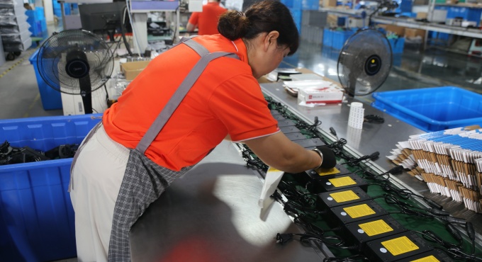 Worker handling finished battery chargers at the final assembly station

