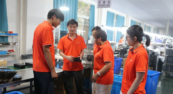 Factory staff checking a battery charger in the packaging area before packing
