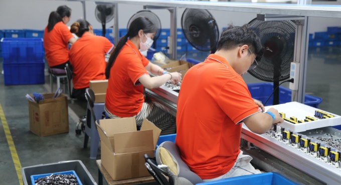 Workers inserting through-hole components into battery charger PCBA boards
