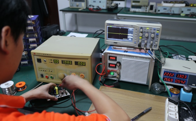 Engineer testing battery charger PCBA performance with laboratory equipment

