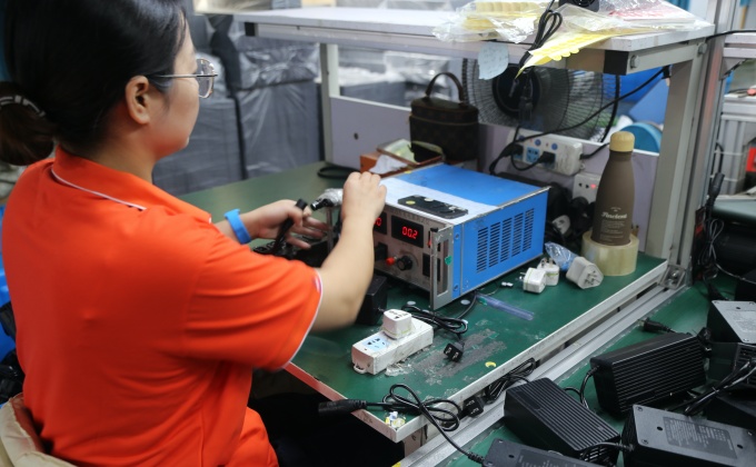 Production worker performing quality testing on finished battery chargers
