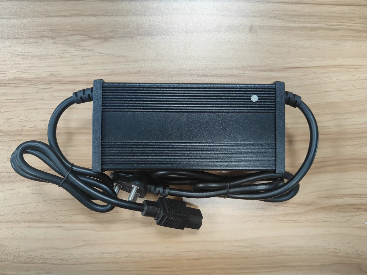 Ribbed black aluminum charger housing with attached cables on a wooden worktop.