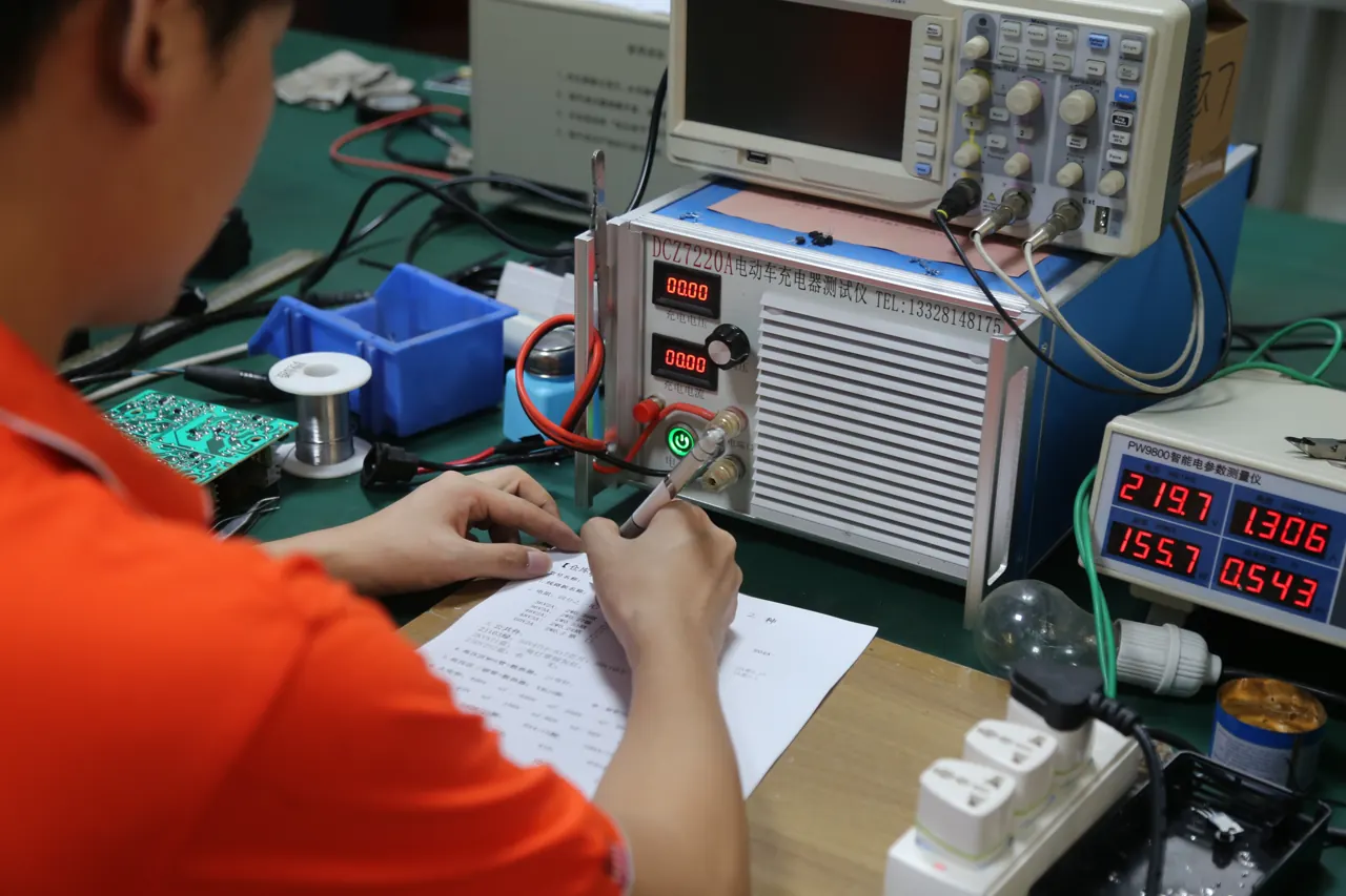 A Linjia technician recording notes at a charger electronics workbench with a test instrument, oscilloscope, power meter and circuit board.