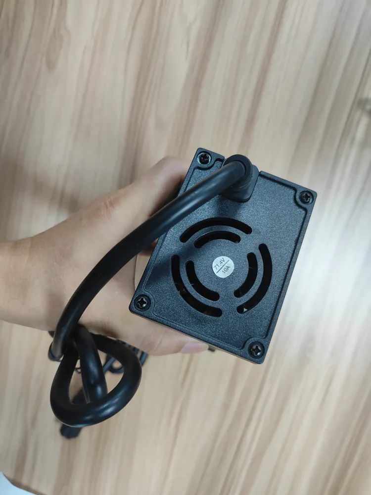 Fan grille and cable exit at the end of a black charger housing held by a worker.