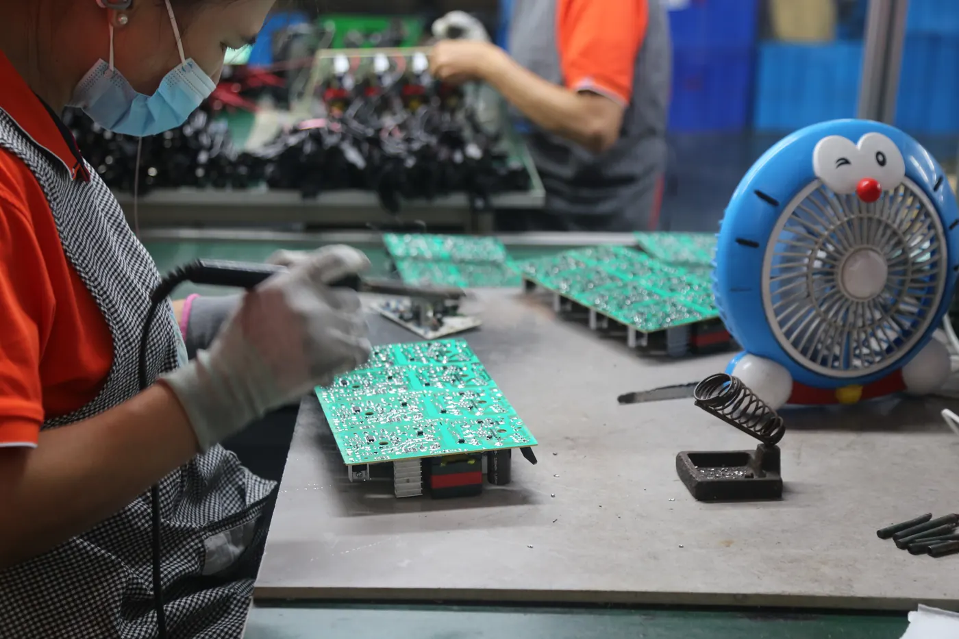 A worker handling a charger circuit board at a Linjia production workbench.