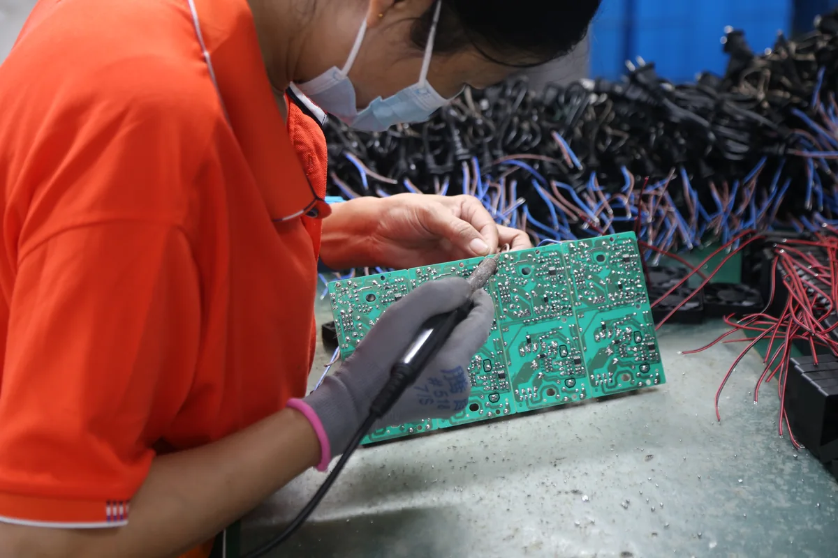 Worker soldering connections on a battery charger circuit board at Linjia's production line